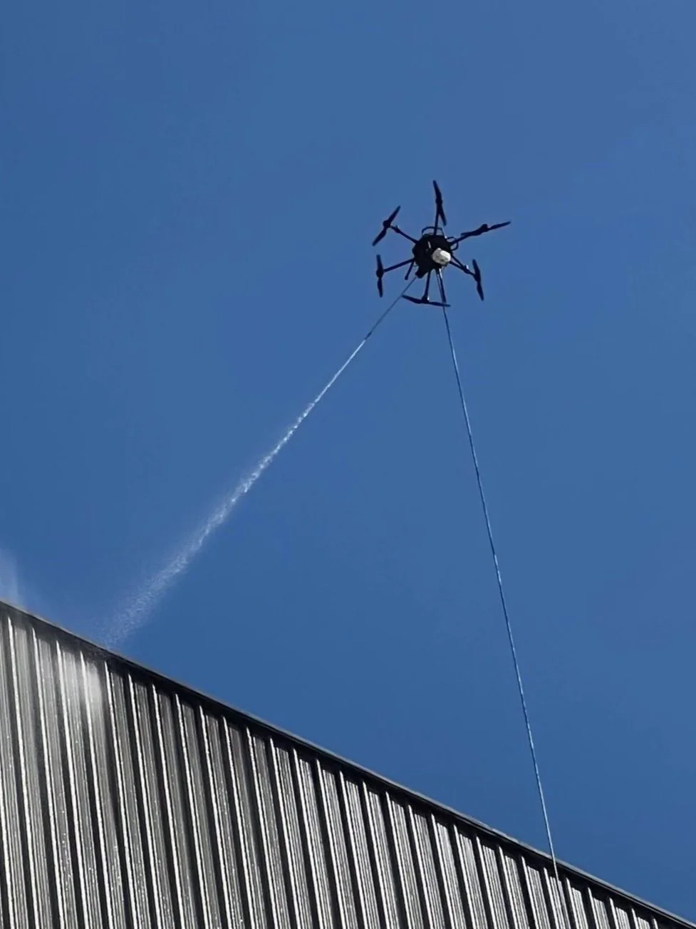High-pressure cleaning drone spraying water on a commercial building roofline
