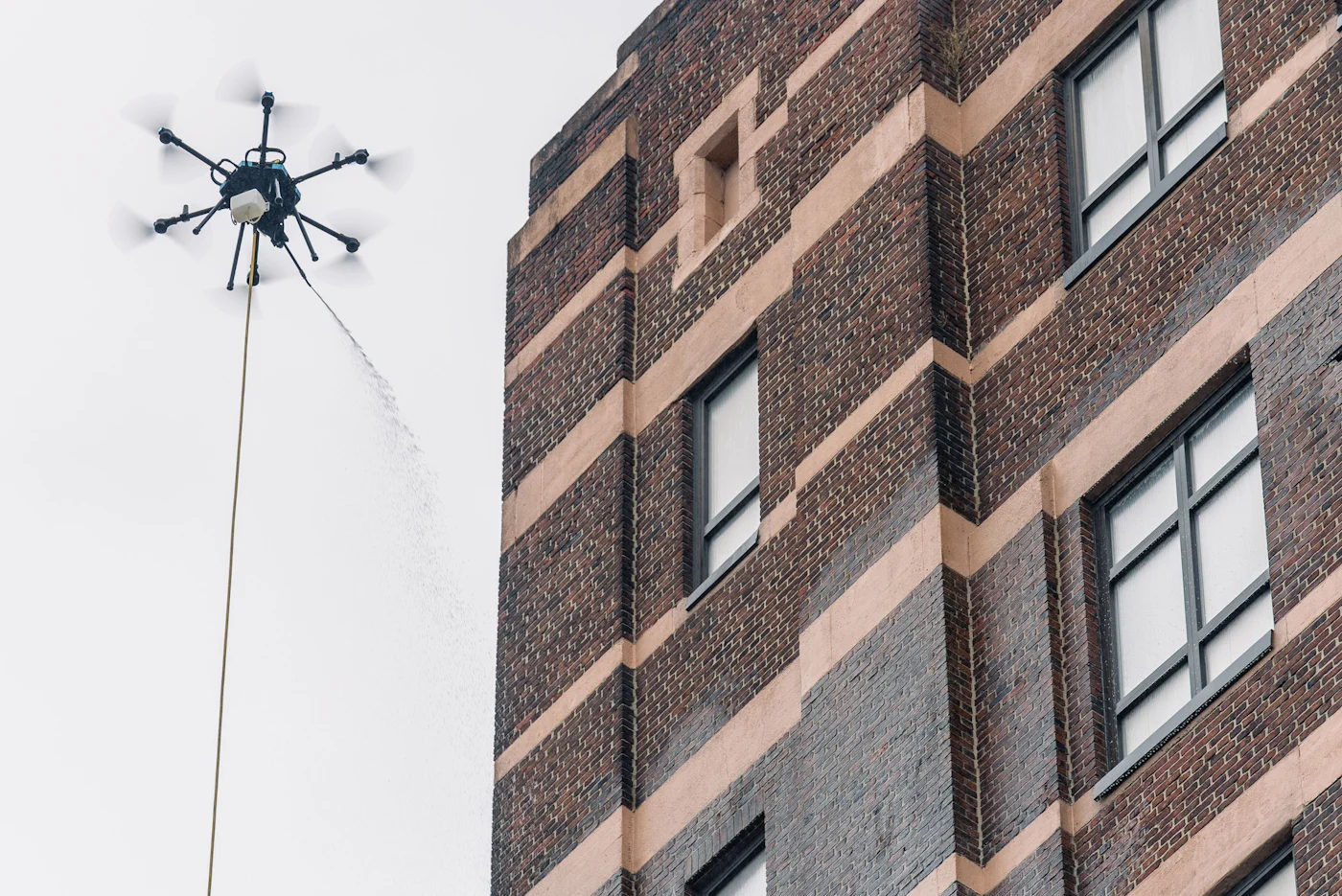 Tethered cleaning drone flying beside a tall brick tower at the Domino Sugar refinery