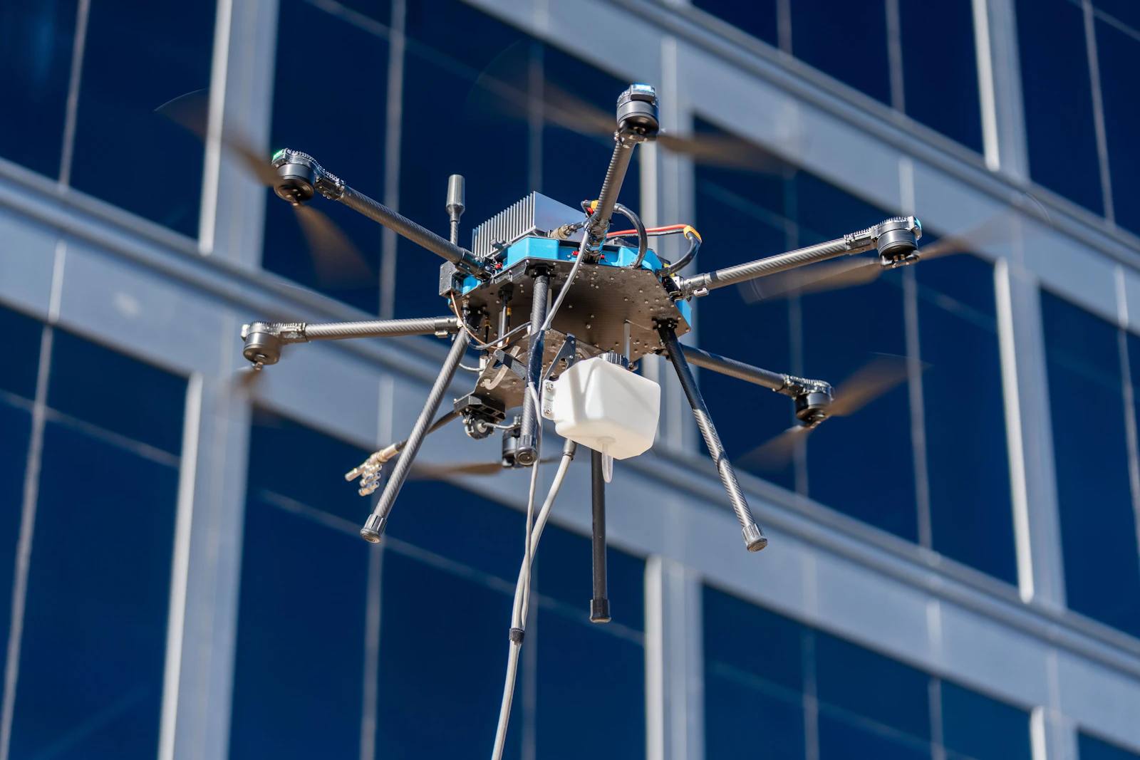 Tethered cleaning drone flying beside the glass facade of a multi-story commercial building