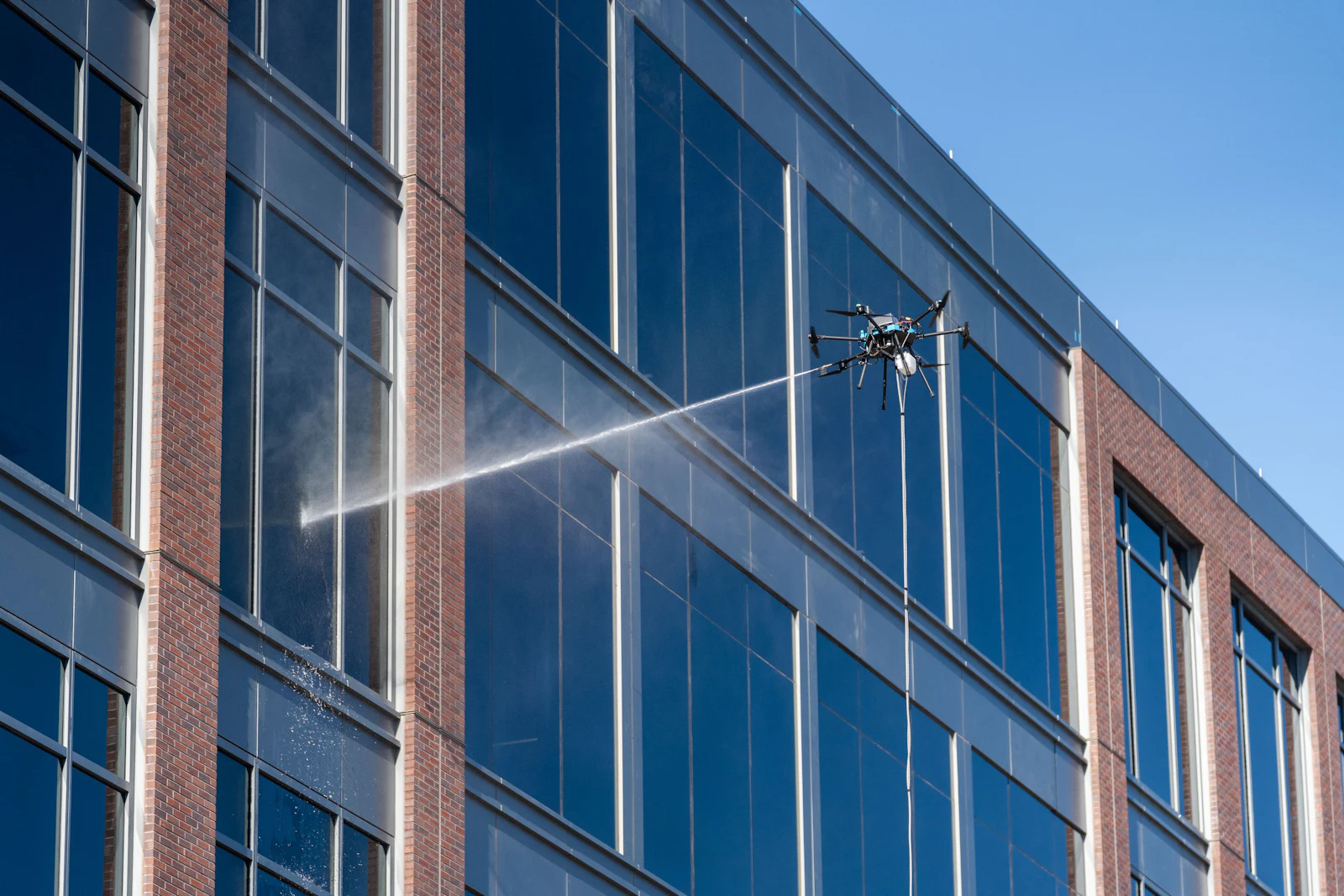 Cleaning drone spraying the glass facade of a multi-story commercial building