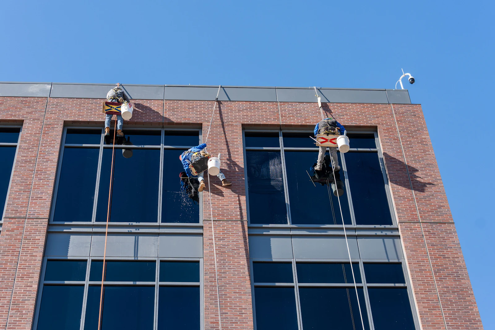 Window cleaners on ropes hanging down a multi-story brick and glass building